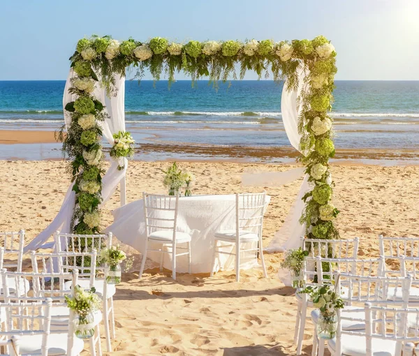 Romantyczna ceremonia ślubna nad oceanem, plaża w słoneczny dzień. Drewniany łuk ozdobiony świeżymi kwiatami. Białe fotele na piasku. — Zdjęcie stockowe