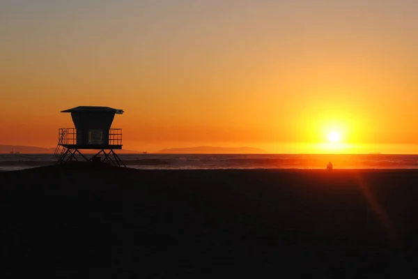 Plavčík věž na kalifornské pláži při západu slunce. Člověk sedí a sledovat západ slunce nad mořem. — Stock fotografie