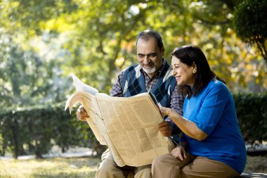 Dışarıda parkta gazete okuyan mutlu yaşlı çift.