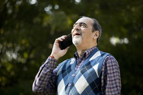 Happy senior man using phone at park