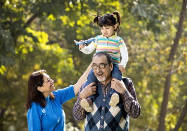 Grandmother with girl holding toy airplane sitting on grandfathers shoulder at park