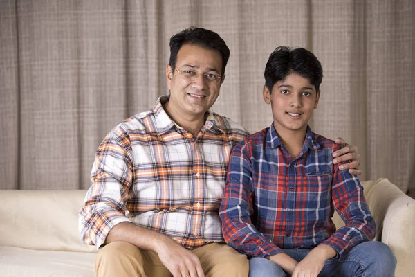 Mutlu baba ve oğul evdeki kanepede otururken kameraya bakıyor.