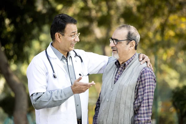 Doctor talking with senior man in hospital garden — Stock Photo, Image
