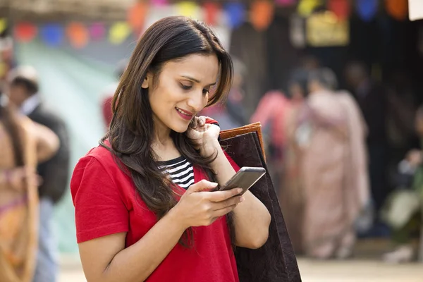 Mujer feliz sosteniendo bolsas de compras y mensajes de texto en el teléfono móvil en el mercado — Foto de Stock