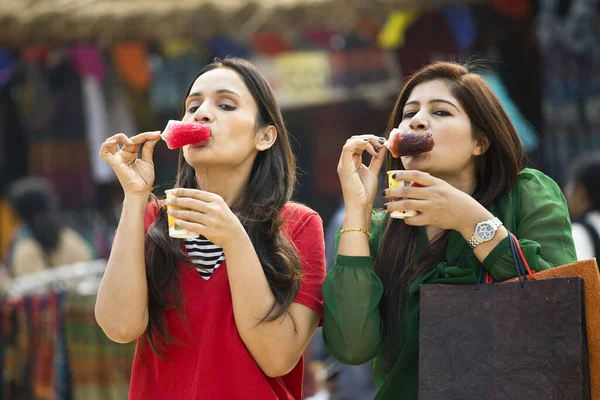 Two women eating flavored ice gola dipped in syrup — ストック写真