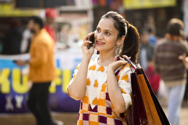 Щаслива жінка тримає сумки і розмовляє на мобільному телефоні на ринку — стокове фото
