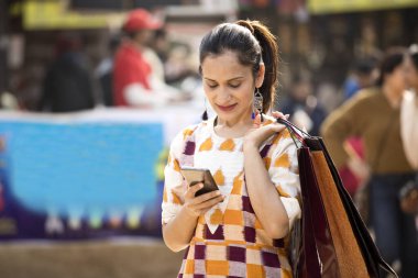 Happy woman holding shopping bags and texting on mobile phone at market