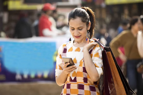 Mujer feliz sosteniendo bolsas de compras y mensajes de texto en el teléfono móvil en el mercado — Foto de Stock