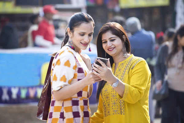Dos mujeres sosteniendo bolsas de compras y mensajes de texto en el teléfono móvil en el mercado — Foto de Stock