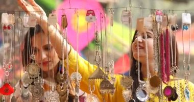 Two women shopping for necklace and earrings at street market
