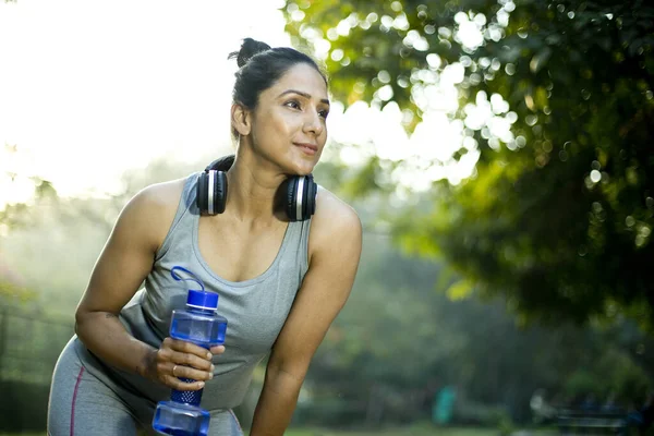 Fit mujer con forma de mancuerna botella de agua y auriculares en el parque — Foto de Stock