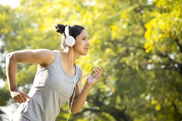 Sporcu kadın müzik dinliyor ve parkta koşuyor.
