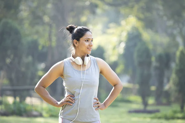 Mujer en ropa deportiva escuchando música en los auriculares en el parque al aire libre — Foto de Stock