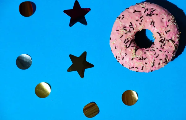 Işıltılı ve konfetili parlak mavi bir arka planda pembe çörek.