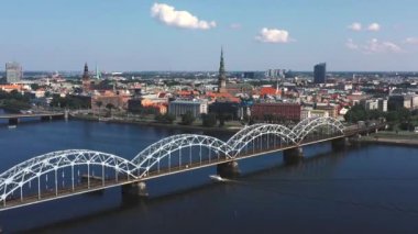 Riga, Letonya - Mayıs 2019: Nehir ve Riga şehir merkezi arasındaki demiryolu köprüsünün panorama manzaralı klibi.