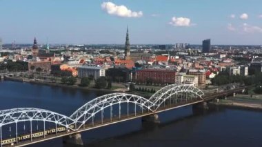 Riga, Letonya - Mayıs 2019: Nehir ve Riga şehir merkezi arasındaki demiryolu köprüsünün panorama manzaralı klibi.
