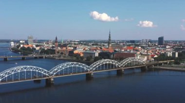 Riga, Letonya - Mayıs 2019: Nehir ve Riga şehir merkezi arasındaki demiryolu köprüsünün panorama manzaralı klibi.