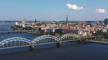 Riga, Letonya - Mayıs 2019: Nehir ve Riga şehir merkezi arasındaki demiryolu köprüsünün panorama manzaralı klibi.