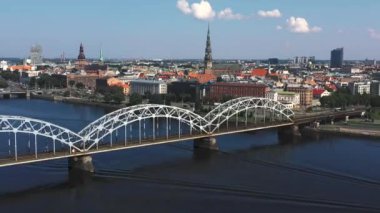 Riga, Letonya - Mayıs 2019: Nehir ve Riga şehir merkezi arasındaki demiryolu köprüsünün panorama manzaralı klibi.