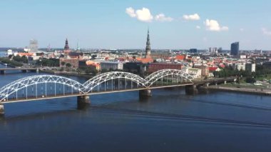 Riga, Letonya - Mayıs 2019: Nehir ve Riga şehir merkezi arasındaki demiryolu köprüsünün panorama manzaralı klibi.