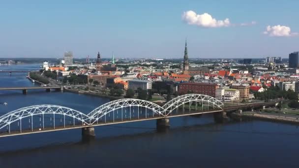 RIGA, LETTONIE - MAI 2019 : Vidéo aérienne avec vue panoramique sur le pont ferroviaire traversant une rivière et le centre-ville de Riga . — Video