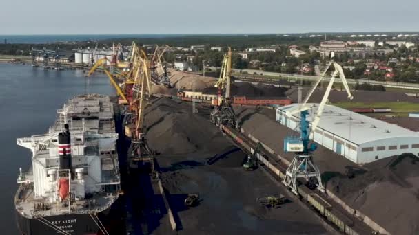 Ventspils, Латвія - липень 2019: Повітряний вид крана, який завантажує вантаж в сухий вантажний корабель і вид на порт. — стокове відео