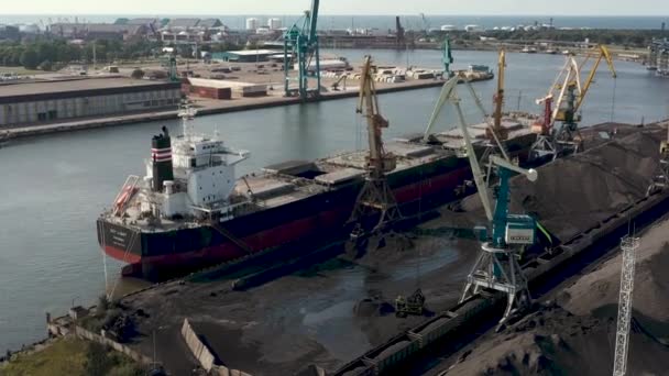 Ventspils, Lotyšsko - červenec, 2019: Letecký pohled na přístavní jeřáb, který nakládá náklad do suché nákladní lodi s výhledem na přístav. — Stock video