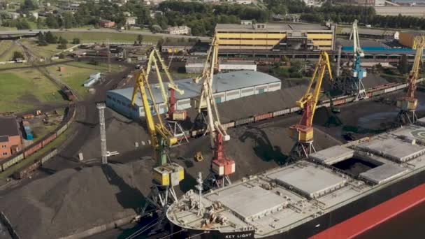 Ventspils, Letland - juli 2019: Luchtfoto van havenkraan die vracht laadt in droog vrachtschip en spoorvervoer. — Stockvideo