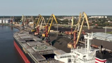 Ventspils, Letonya - Temmuz 2019: Ventspils limanındaki kargoyu yükleyen büyük kuru kargo gemisi ve iskele vinçlerinin hava görüntüsü.