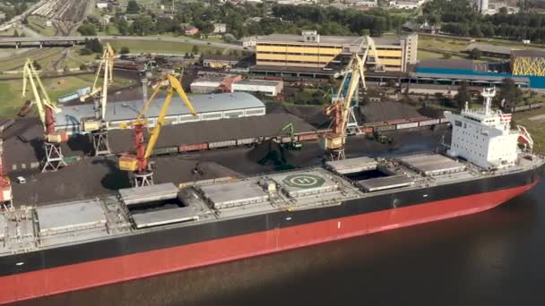 VENTSPILS, Letonia - JULIO, 2019: Vista aérea de grúa portuaria que carga carga carga en buque de carga seca y transporte ferroviario . — Vídeos de Stock