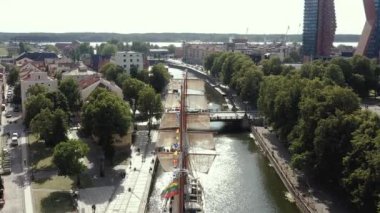 KLAIPEDA, LITHUANIA - JULY, 2019: Aerial view of the sailboat Meridianas in the river Dane and cityscape of Klaipeda.