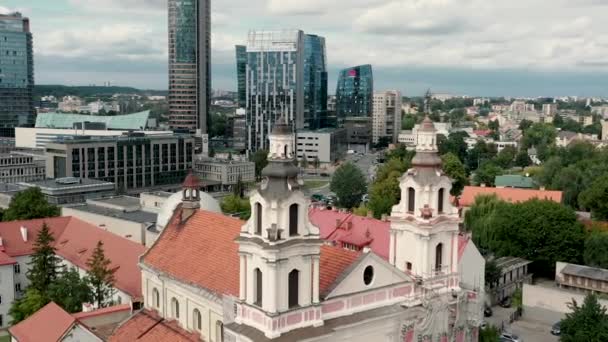 VILNIUS, LITHUANIA - JULY, 2019: Aerial view of the towers of church of Archangel Raphael near business city centers. — ストック動画