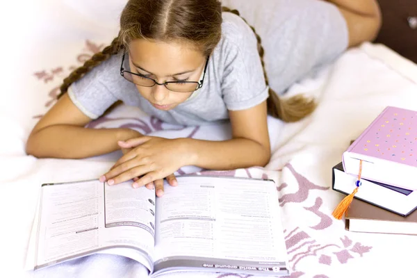 Jong meisje met bril lezen boek op het bed — Stockfoto