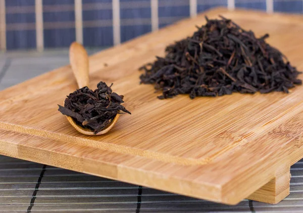 Chá friável preto em uma colher de madeira e em uma bandeja de madeira — Fotografia de Stock