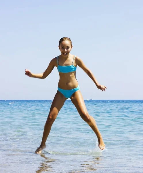 Ung söt leende flicka i blå baddräkt hoppa i havet — Stockfoto