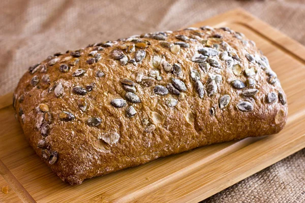 Ржаной хлеб с тыквенными семечками на деревянном блюде на мешковине — стоковое фото
