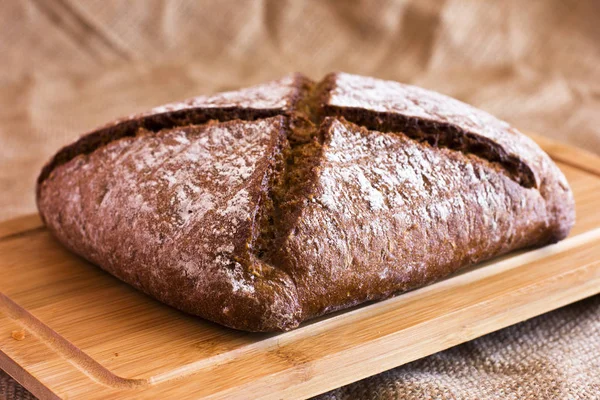 Pão escuro de centeio em uma travessa de madeira na serapilheira — Fotografia de Stock