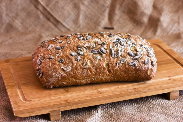 Pão de centeio com sementes de abóbora em uma bandeja de madeira na serapilheira — Fotografia de Stock