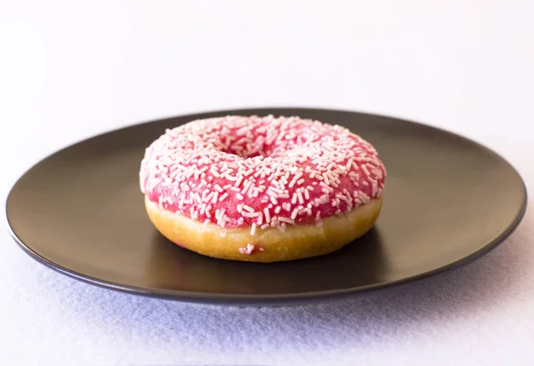 Leuchtend rosa Donut auf schwarzem Keramikteller auf weißem Hintergrund — Stockfoto