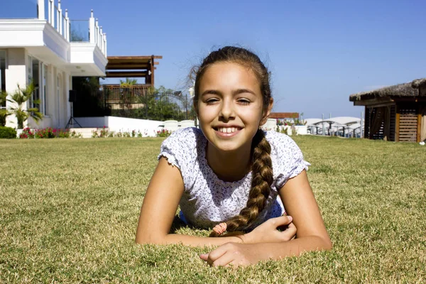 Όμορφη νεαρή κοπέλα βρίσκεται σε ένα στομάχι στο γρασίδι και χαμογελαστός — Φωτογραφία Αρχείου
