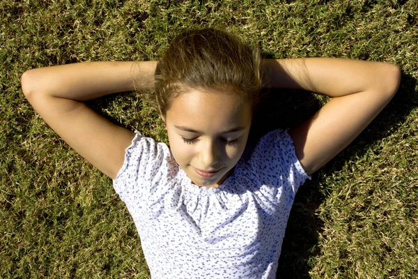 A young girl lies on the mown grass stretching her arms
