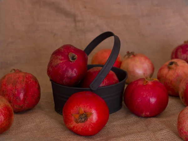 Ripe red pomegranates in a metal black bowl on a brown burlap — Stock Photo, Image