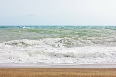 Fırtınalı denizde ve mavi gökyüzü, beyaz deniz köpüğü bir sarı kum plajındaki.