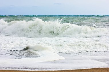 Fırtınalı denizde ve mavi gökyüzü, beyaz deniz köpüğü bir sarı kum plajındaki.