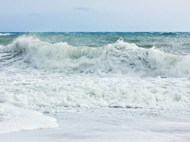 Fırtınalı denizde ve mavi gökyüzü, beyaz deniz köpüğü bir sarı kum plajındaki.
