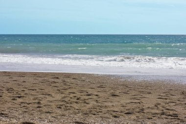 Yaz deniz ve mavi gökyüzü, beyaz deniz köpüğü bir sarı kum plajındaki.