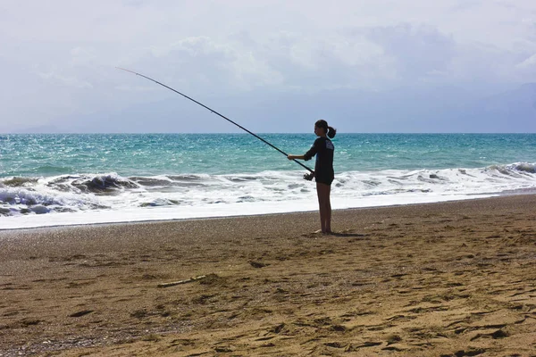 Ung flicka är fiske på stranden på blå havet — Stockfoto