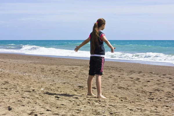 En ung flicka står på stranden nära havets blåa — Stockfoto