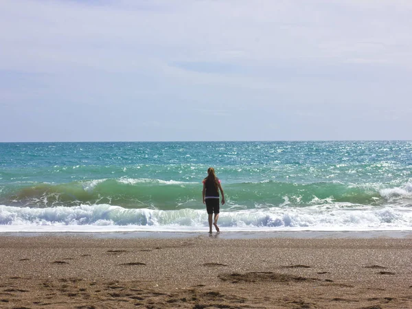En ung flicka står på stranden nära havets blåa — Stockfoto