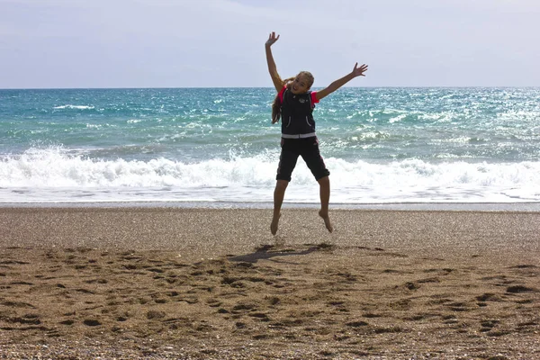 Chica joven corre y salta en la playa cerca del mar azul —  Fotos de Stock